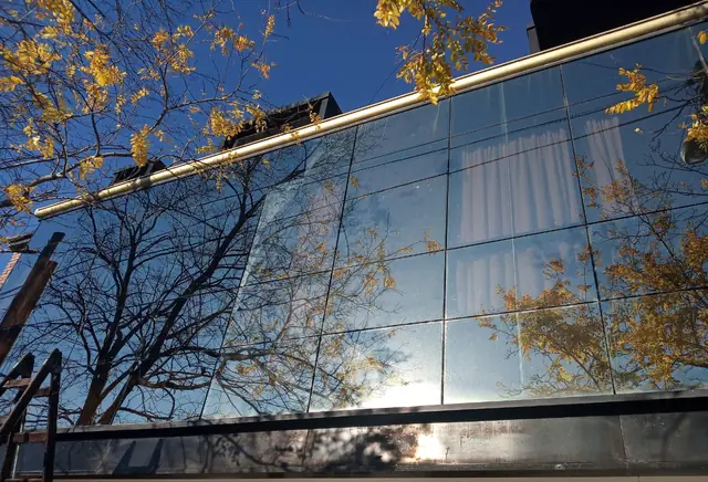 Baranda de vidrio reflejando el cielo y un árbol